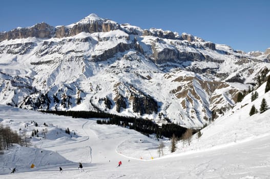 view from above of steep ski run in dolomites, shot in bright winter light, in background high valley and mountains