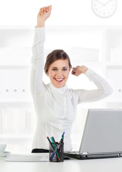 Happy young businesswoman at her desk raises her hands