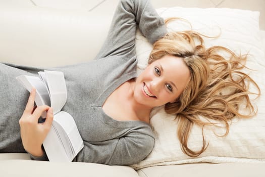High angle view on smiling blond woman lying on sofa with book