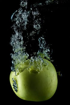 A green apple splashing on a water surface with a black background.