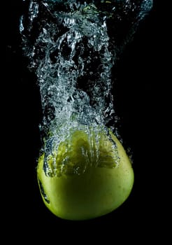 A green apple splashing on a water surface with a black background.