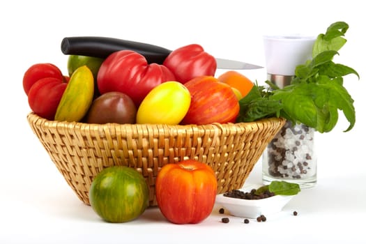 A basket with many different organic tomatoes,salt and pepper mill and a knife in front of a white background. A basket with a variety of organic tomatoes,salt and pepper mill and a knife in front of white background.