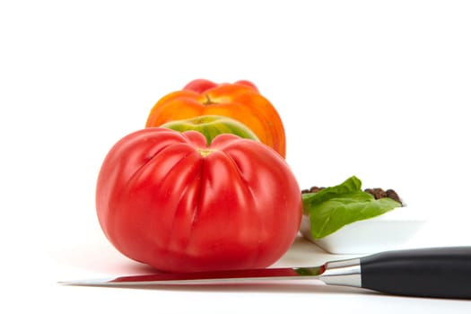 Four large organic tomatoes in a row with pepper peel and a knife in front of it. Four large organic tomatoes in a bowl with pepper set and a knife in front.