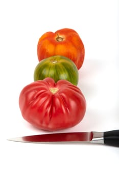 Three large organic tomatoes in a row with a knife in front of them. Three large organic tomatoes in a row with a knife before.