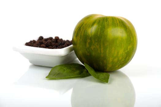 Green Zebra tomato with a small bowl of peppercorns as a close-up. Green Zebra tomato variety with a small bowl of peppercorns as a close-up.