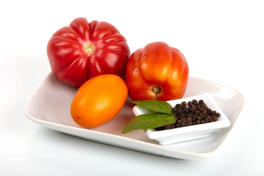 Three organic tomatoes in a bowl with peppercorns and basil leaves. Three organic tomatoes in a bowl with pepper and basil leaves.