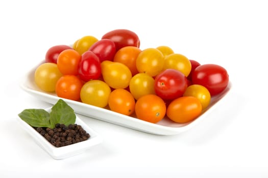 White bowl with small,colourful organic tomatoes and a small bowl with peppercorns and basil leaves. Small white bowl with colorful organic tomatoes and a bowl with pepper and basil leaves.