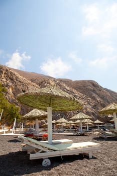 Beach umbrellas and sunbeds in morning sun in Perissa beach, Santorini, Greece