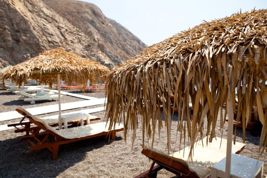 Beach umbrellas and sunbeds in morning sun in Perissa beach, Santorini, Greece