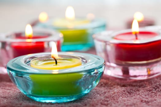 Close-up of yellow and red candles in glass holders on pink sand