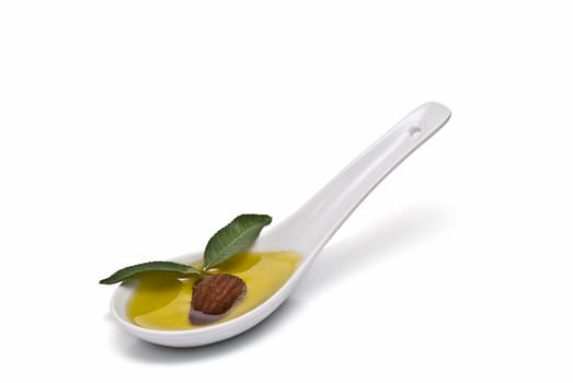 Almonds and a spoon with its oil over a white background.