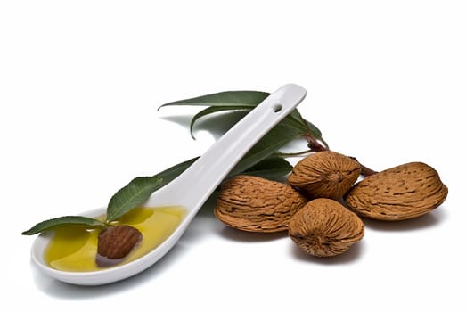 Almonds and a spoon with its oil over a white background.