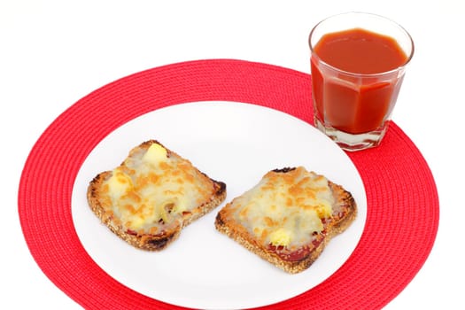 Two healthy slices of sprouted grain bread topped with pizza toppings on a white plate and one glass of vegetable tomato juice on a round red place mat.