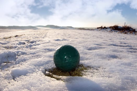 green ball on a snow covered links golf course in ireland in winter