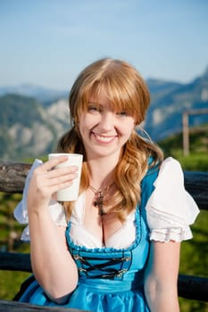 joyful girl in traditional dirndl with cup of milk