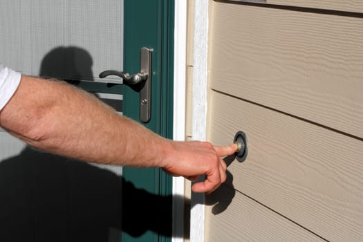 Right hand of a man ringing the front doorbell of a home.