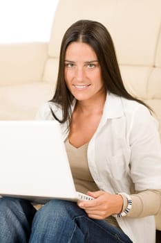 Attractive woman with laptop sitting by couch smiling