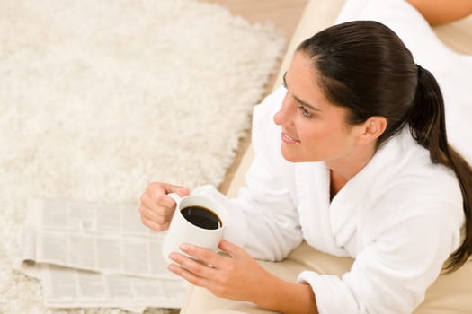 Attractive woman in white bathrobe with coffee newspapers in lounge