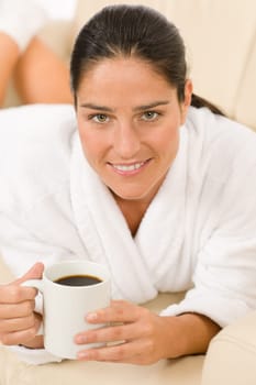 Attractive woman in white bathrobe with coffee in lounge