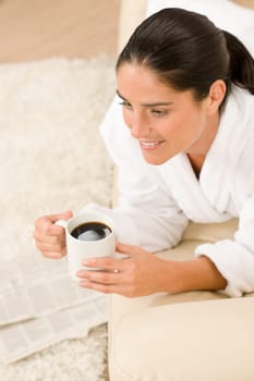 Attractive woman in white bathrobe with coffee newspapers in lounge
