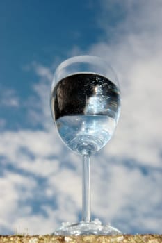 a glass of water on a wall against a bright cloudy blue sky background
