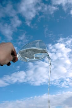 a glass of water being poured against a bright cloudy blue sky background