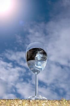 a glass of water on a wall against a bright sunny cloudy blue sky background