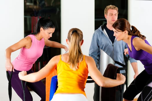Women and trainers in gym in front of exercise machine