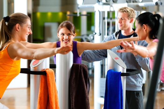 Women and trainers in gym in front of exercise machine