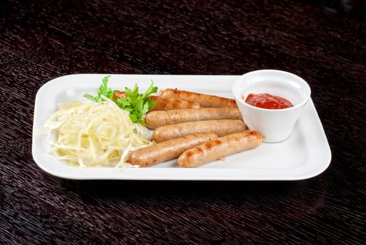 Grilled sausages with cabbage, greens and tomato sauce on white plate