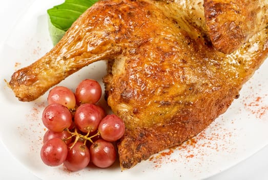 Half roasted chicken closeup with grape and greens on a white