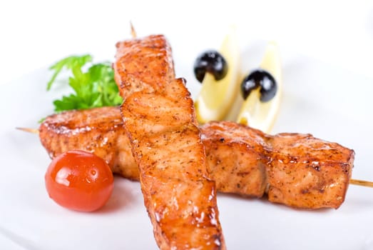 salmon kebab at plate with green lettuce and lemon on a white