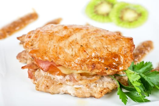 Cooked pork chop on a white plate with kiwi and parsley