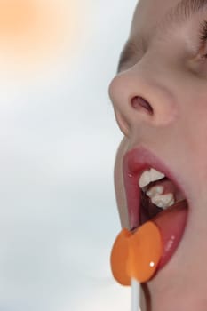 young girl licking an orange lollipop into a heart shape on a sunny day