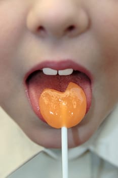 young girl licking an orange lollipop into a heart shape