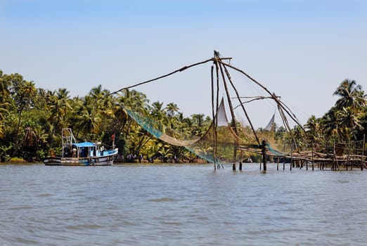 North Paravoor, Gothuruth, Kerala, India, Asia - September 25th, 2011: Landscape fishing nets and passenger boat in Kerala backwaters lakes, spectators to the races, police marshalls, horizontal crop space copy space blue sky reflections on the water surf
