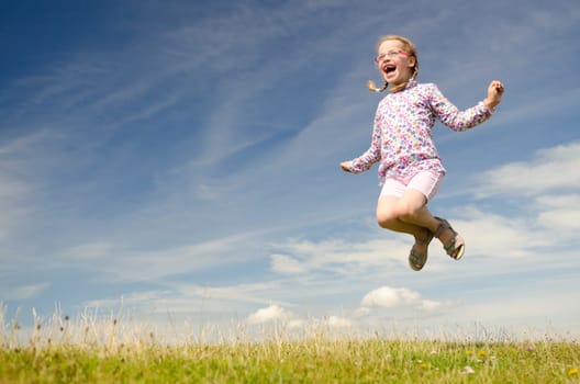 Young girl jumping on a green meadow against blue sky