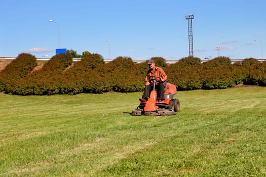 Mature man driving grass cutter in a sunny day