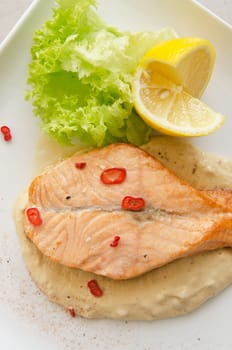 Grilled salmon steak with greens, lemon, sauce and pepper chile