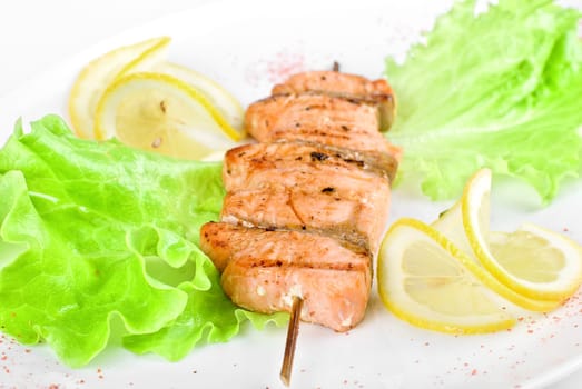 salmon kebab at plate with green lettuce and lemon on a white