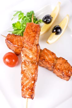 salmon kebab at plate with green lettuce and lemon on a white