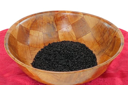 Dry organic black purple rice in a wood bowl on a red placemat.