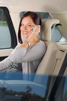 Executive attractive female manager sitting in car backseat calling phone