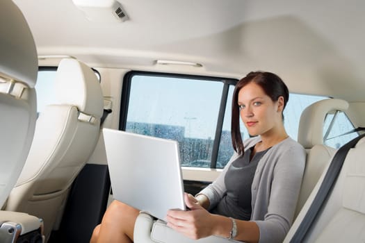 Executive woman manager working on laptop sitting car leather backseat