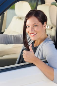 Attractive elegant businesswoman driving luxury new car thumb up smiling