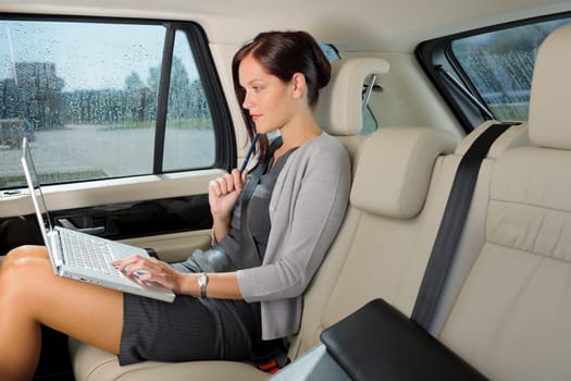 Executive woman manager working on laptop sitting car leather backseat