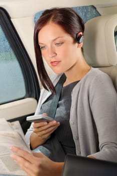 Attractive executive businesswoman sitting in car calling phone checking newspapers
