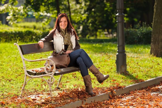 Autumn fashion outfit attractive woman sitting on park bench sunset