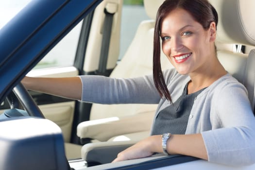 Attractive elegant businesswoman driving luxury car smiling at camera