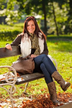 Autumn fashion outfit attractive woman sitting on park bench sunset
